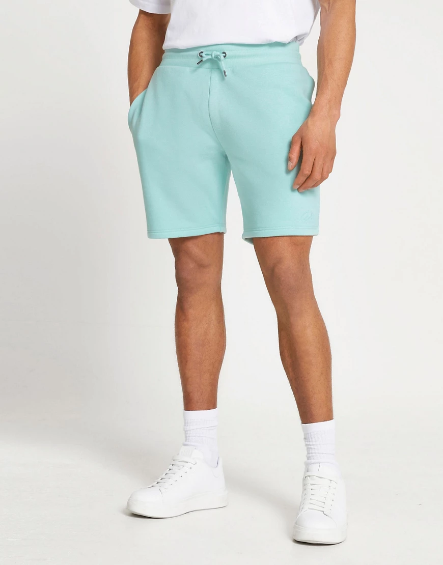 River Island – Schmal geschnittene Jersey-Shorts in Grün mit „RI“-Logo günstig online kaufen